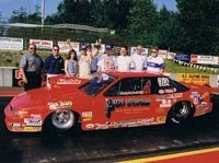 A red drag car with a group of people at the track
